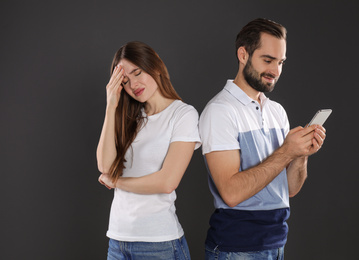 Photo of Man with smartphone ignoring his girlfriend on black background. Relationship problems