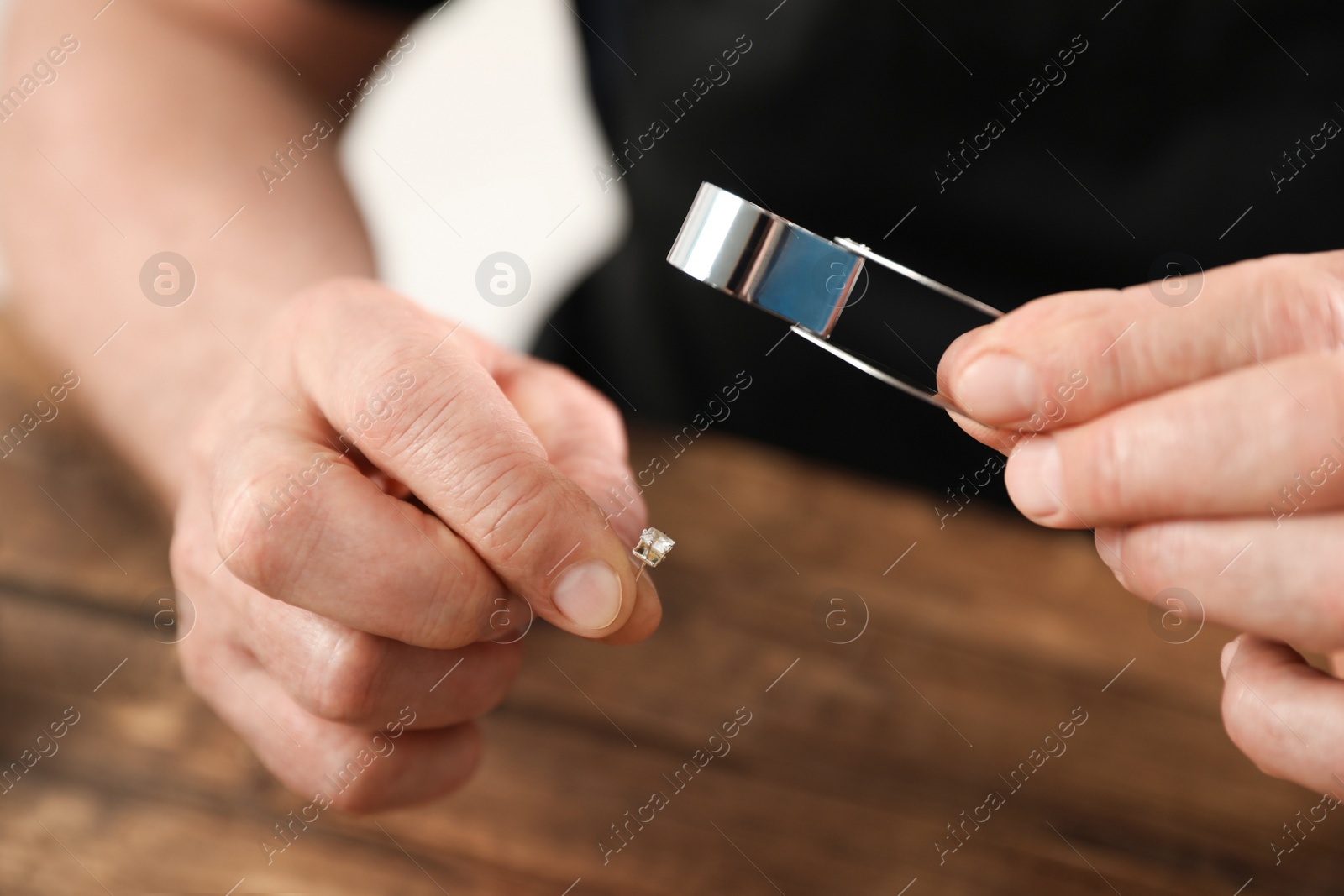 Photo of Male jeweler evaluating earring at table in workshop, closeup