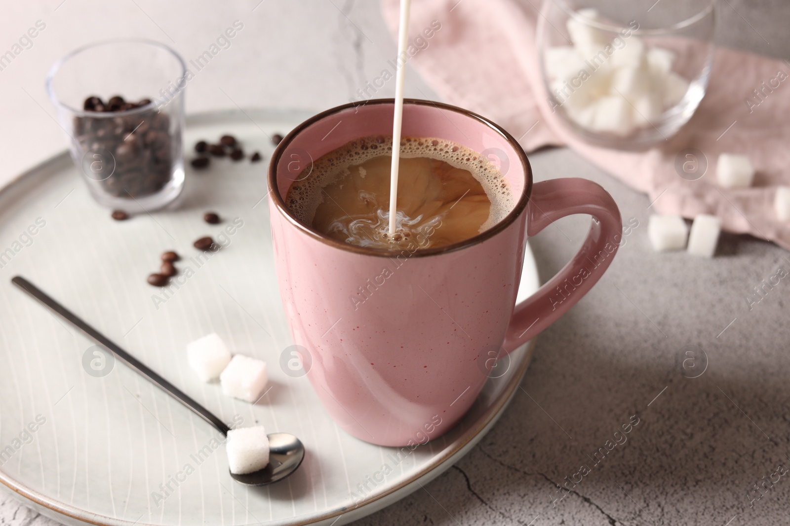 Photo of Pouring milk into cup with coffee on light grey textured table, closeup