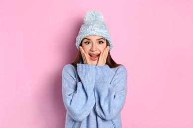 Emotional woman wearing warm sweater and hat on pink background. Winter season