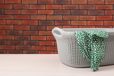 Photo of Plastic laundry basket with clothes near brick wall. Space for text