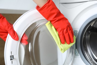 Photo of Woman cleaning washing machine with rag indoors, closeup