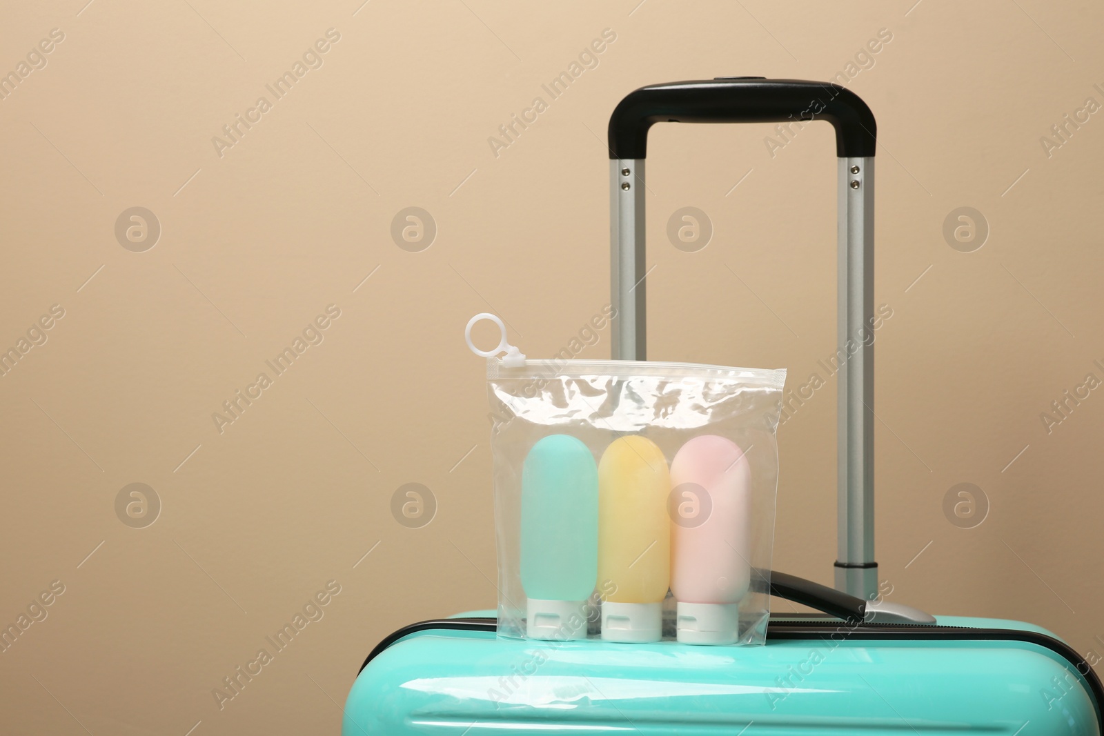 Photo of Cosmetic travel kit in plastic bag on suitcase against beige wall, space for text. Bath accessories