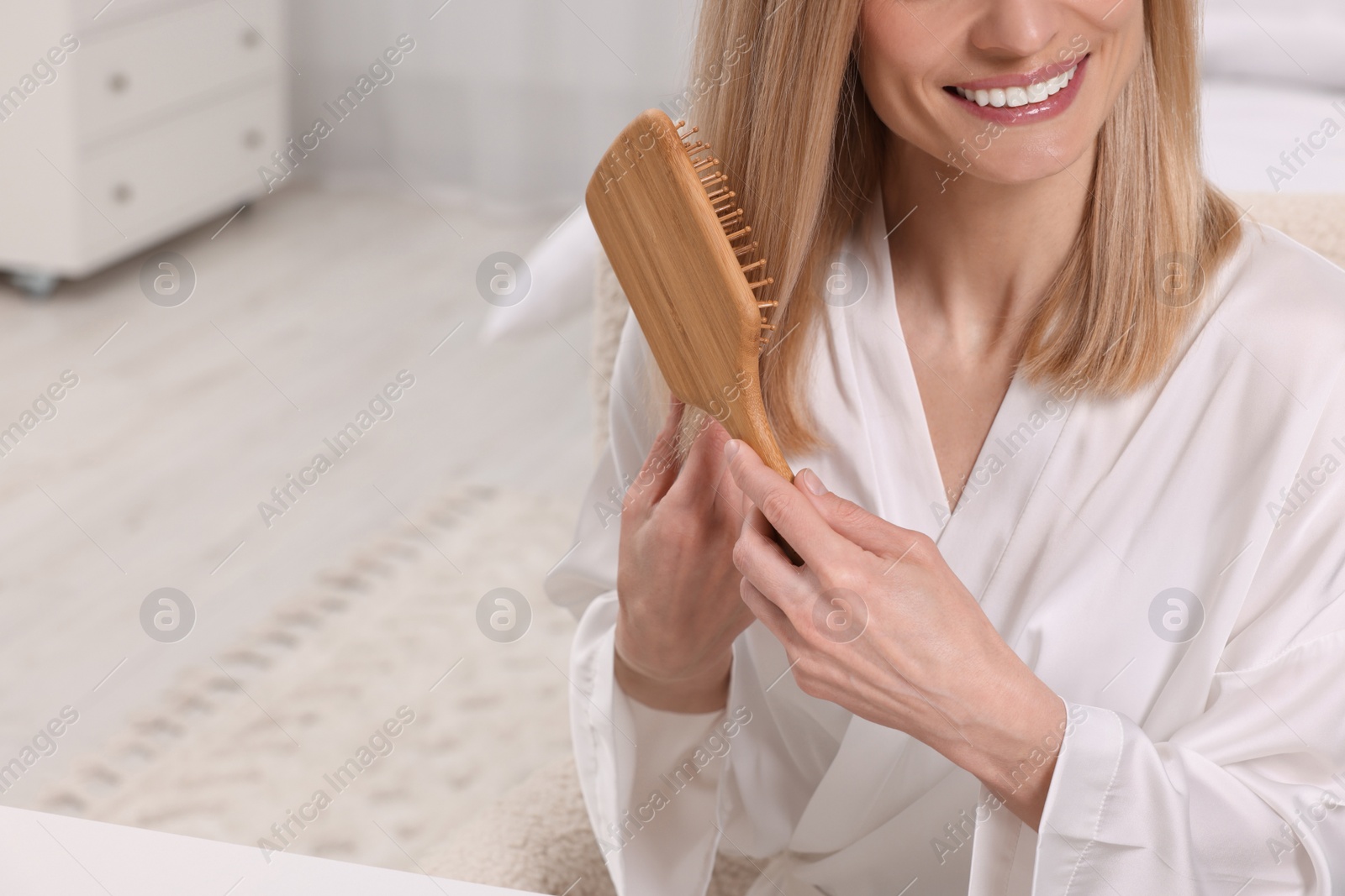 Photo of Happy woman brushing her hair indoors, closeup. Space for text