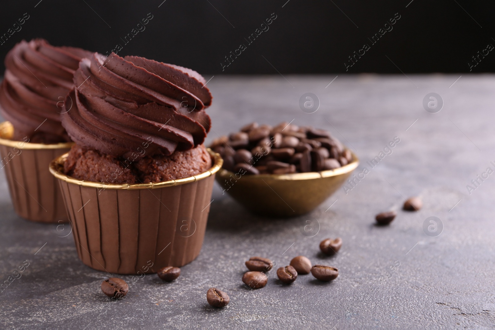 Photo of Delicious chocolate cupcakes and coffee beans on grey textured table, closeup. Space for text