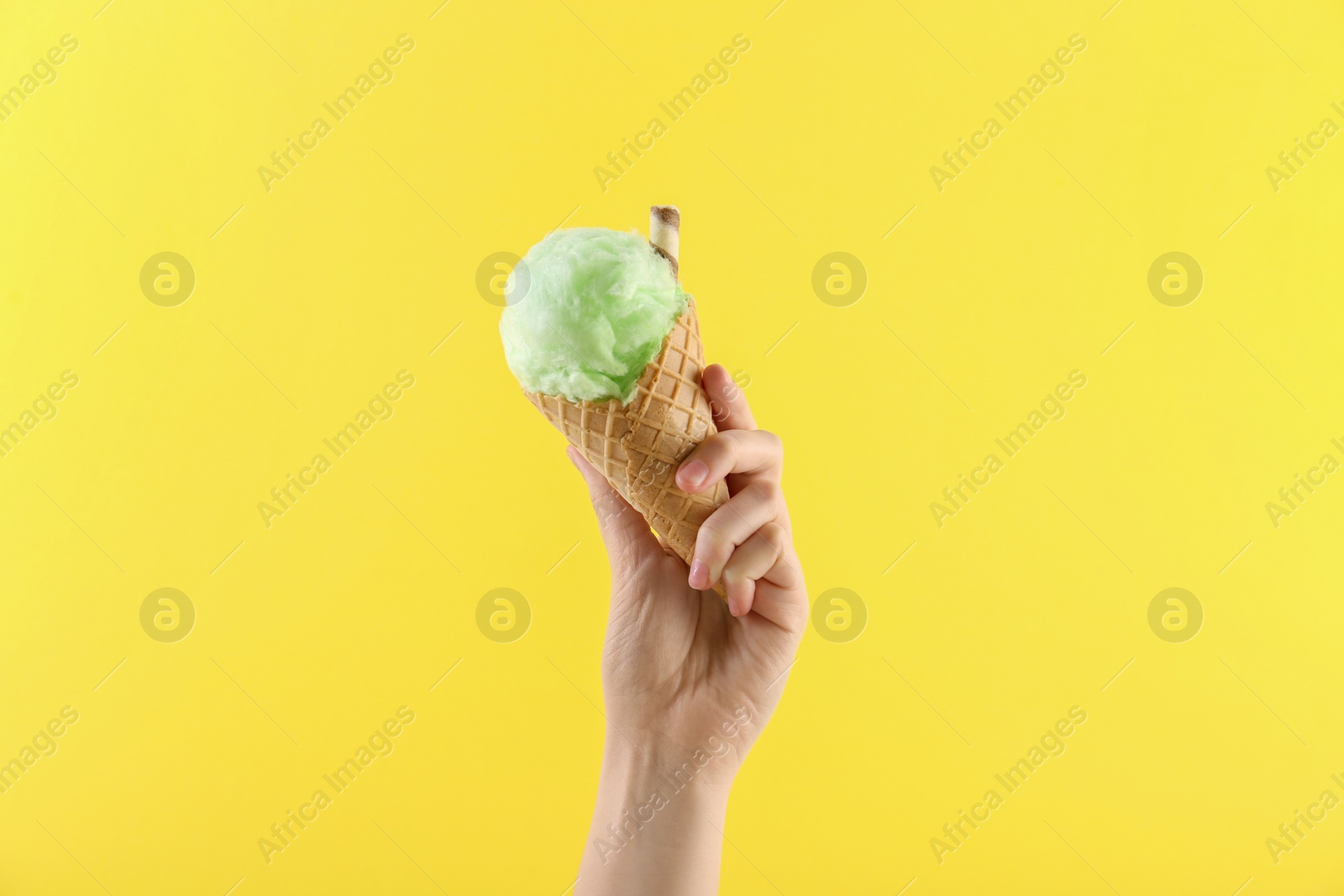 Photo of Woman holding waffle cone with cotton candy on yellow background, closeup