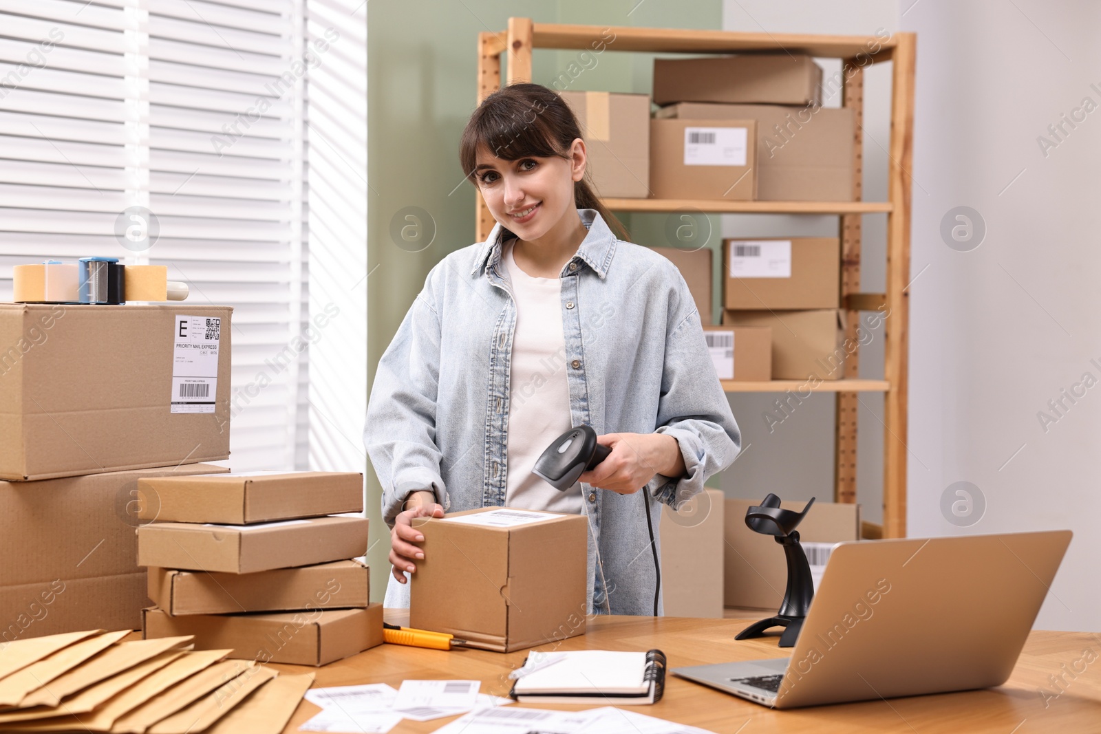 Photo of Parcel packing. Post office worker with scanner reading barcode at wooden table indoors