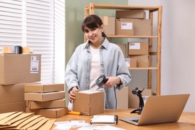 Photo of Parcel packing. Post office worker with scanner reading barcode at wooden table indoors