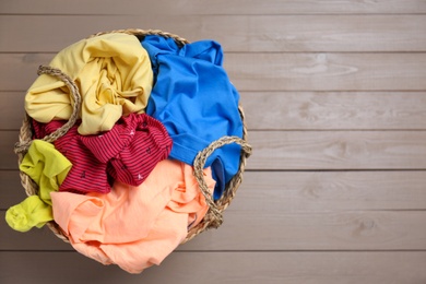 Photo of Wicker laundry basket with different clothes on wooden background, top view. Space for text