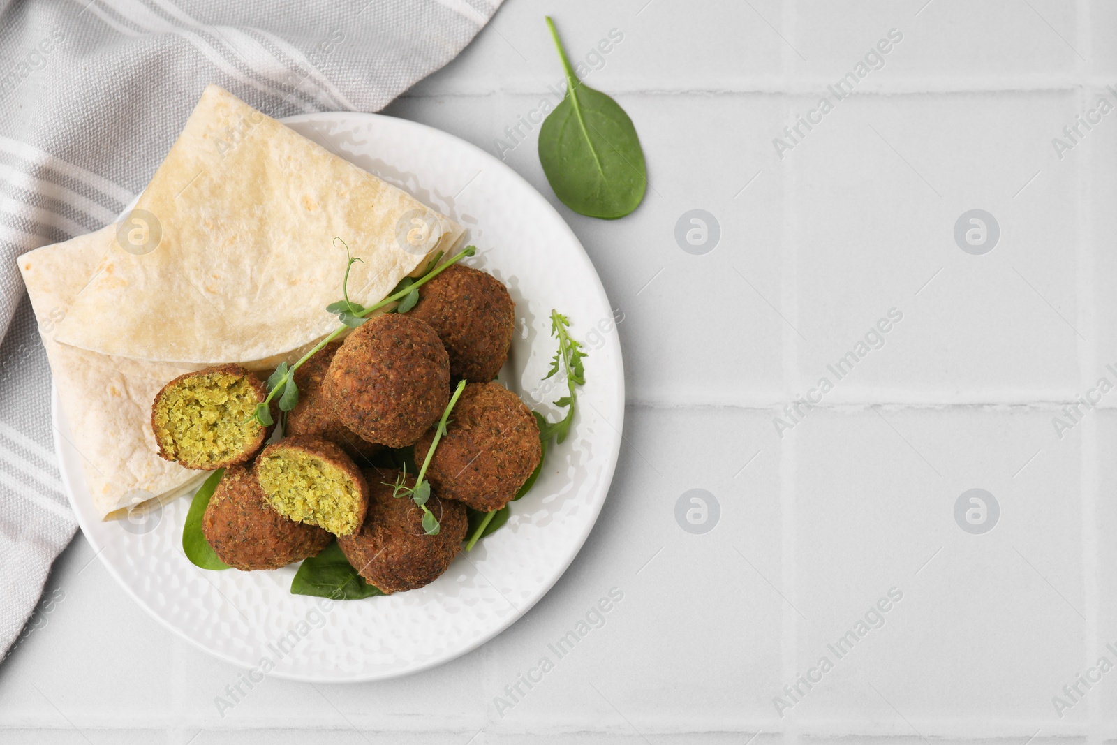 Photo of Delicious falafel balls, herbs and lavash on white tiled table, top view. Space for text