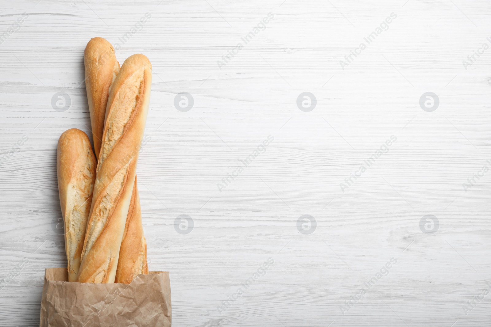 Photo of Tasty baguettes in package on white wooden table, top view. Space for text