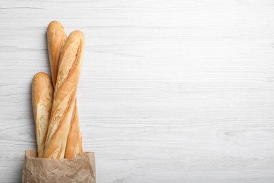 Photo of Tasty baguettes in package on white wooden table, top view. Space for text