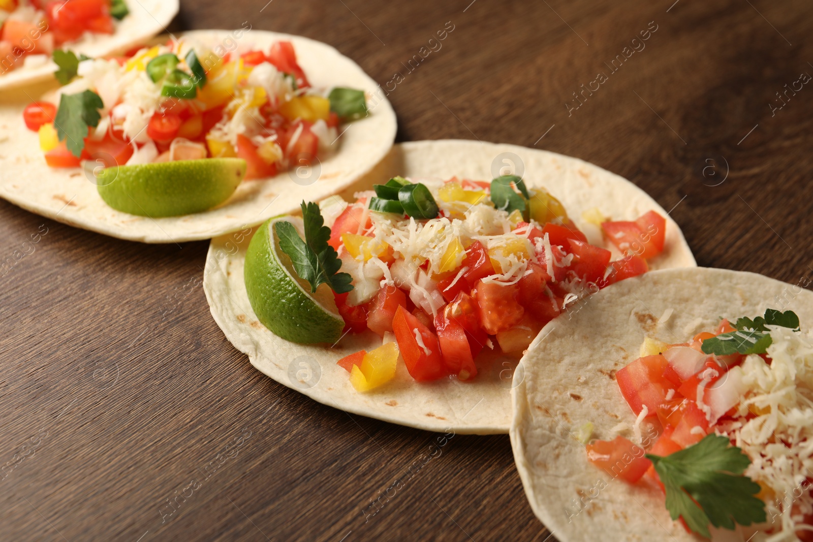 Photo of Delicious tacos with vegetables and lime on wooden table, closeup