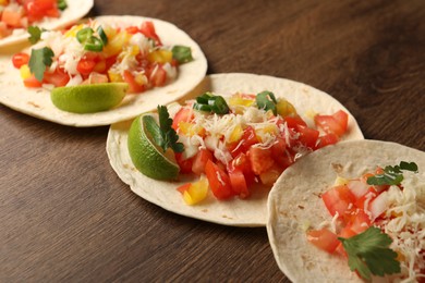 Photo of Delicious tacos with vegetables and lime on wooden table, closeup