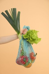 Photo of Woman with string bag of fresh vegetables on beige background, closeup