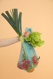 Woman with string bag of fresh vegetables on beige background, closeup