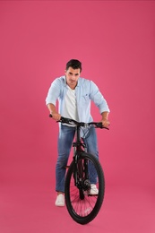 Handsome young man with modern bicycle on pink background