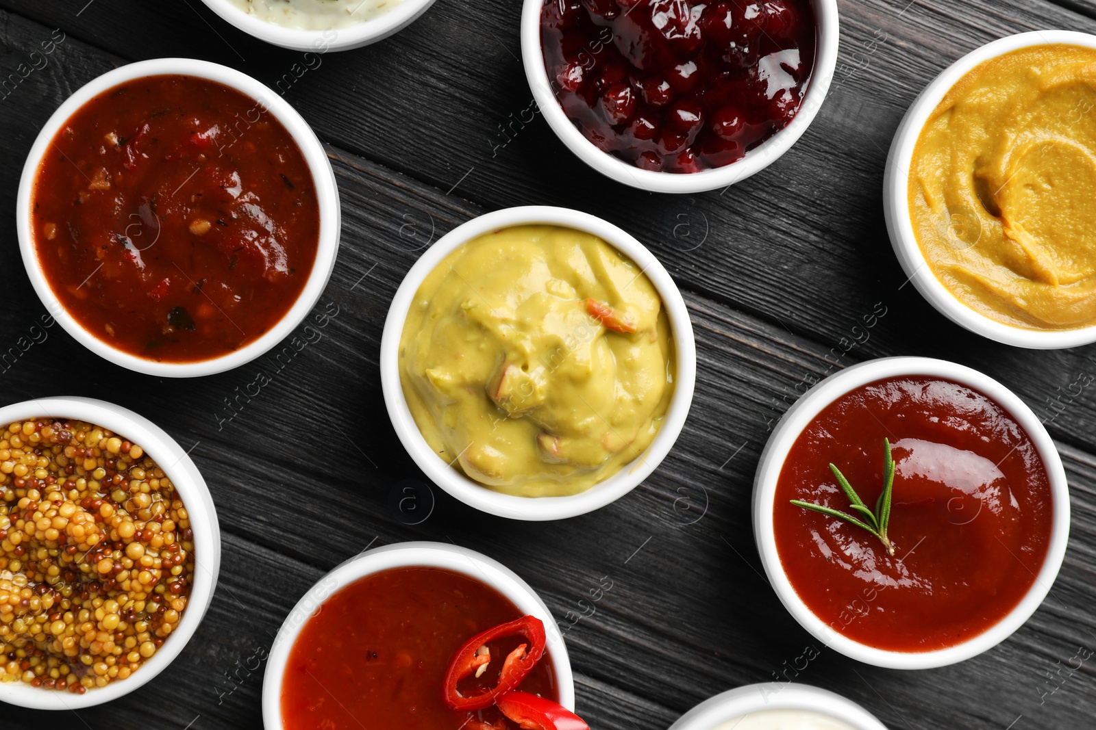 Photo of Different tasty sauces in bowls on black wooden table, flat lay
