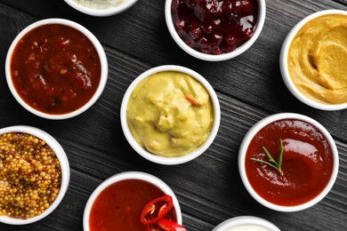 Photo of Different tasty sauces in bowls on black wooden table, flat lay