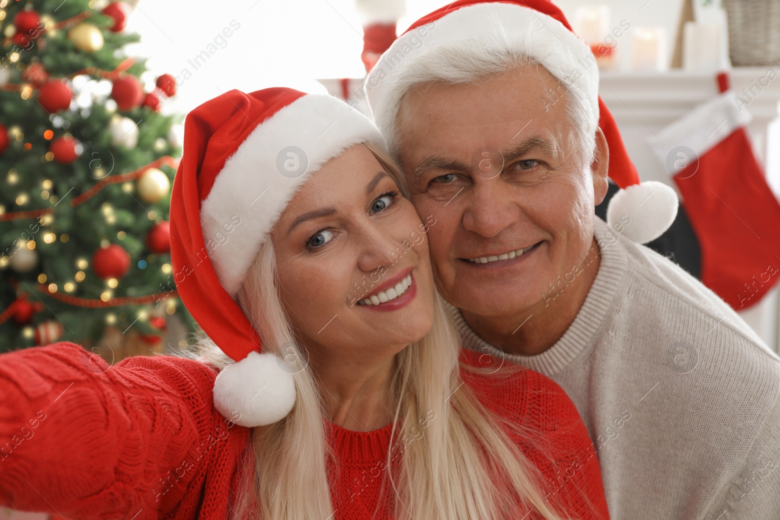 Photo of Happy mature couple in Santa hats taking selfie at home. Christmas celebration