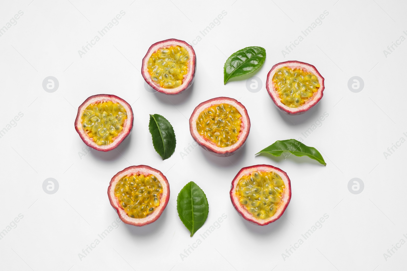 Photo of Halves of passion fruits (maracuyas) and green leaves on white background, flat lay