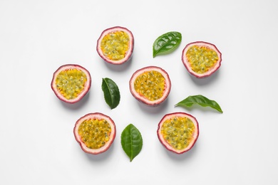 Halves of passion fruits (maracuyas) and green leaves on white background, flat lay