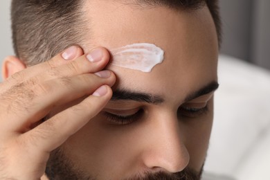 Photo of Man with dry skin applying cream onto his forehead on light background