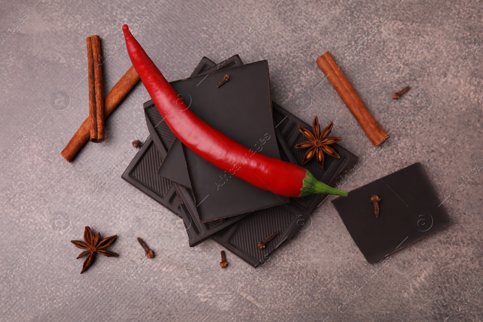 Photo of Delicious chocolate, fresh red chili pepper and spices on grey textured table, flat lay