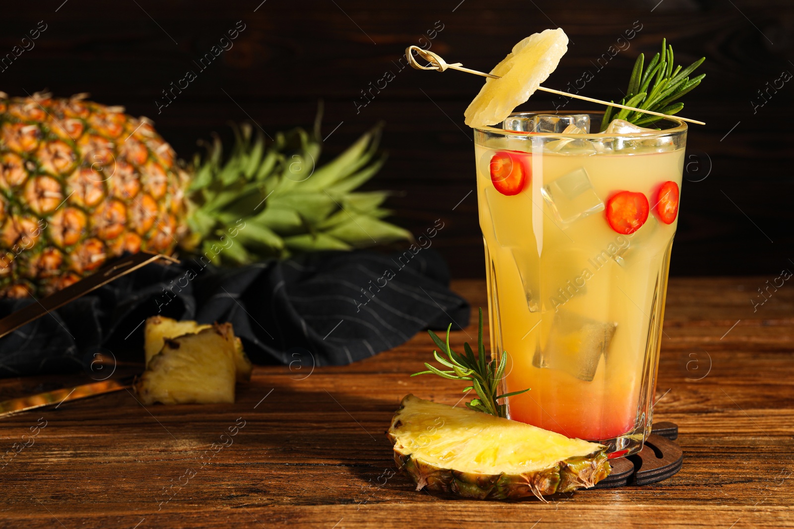Photo of Spicy pineapple cocktail with chili pepper, rosemary and fresh fruit on wooden table