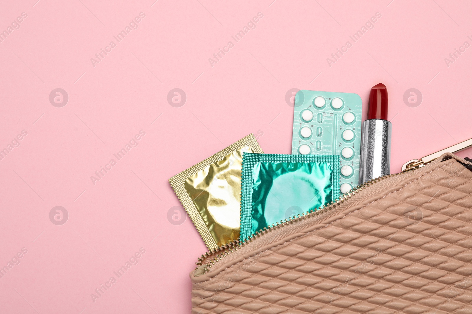 Photo of Condoms, birth control pills and lipstick in purse on pink background, top view with space for text. Safe sex