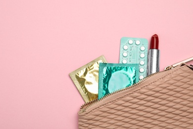 Photo of Condoms, birth control pills and lipstick in purse on pink background, top view with space for text. Safe sex