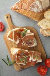 Photo of Tasty sandwiches with cured ham, rosemary and tomatoes on grey table, flat lay