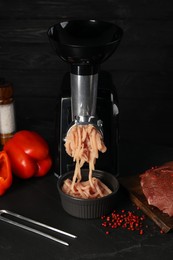Electric meat grinder with chicken mince and products on black table