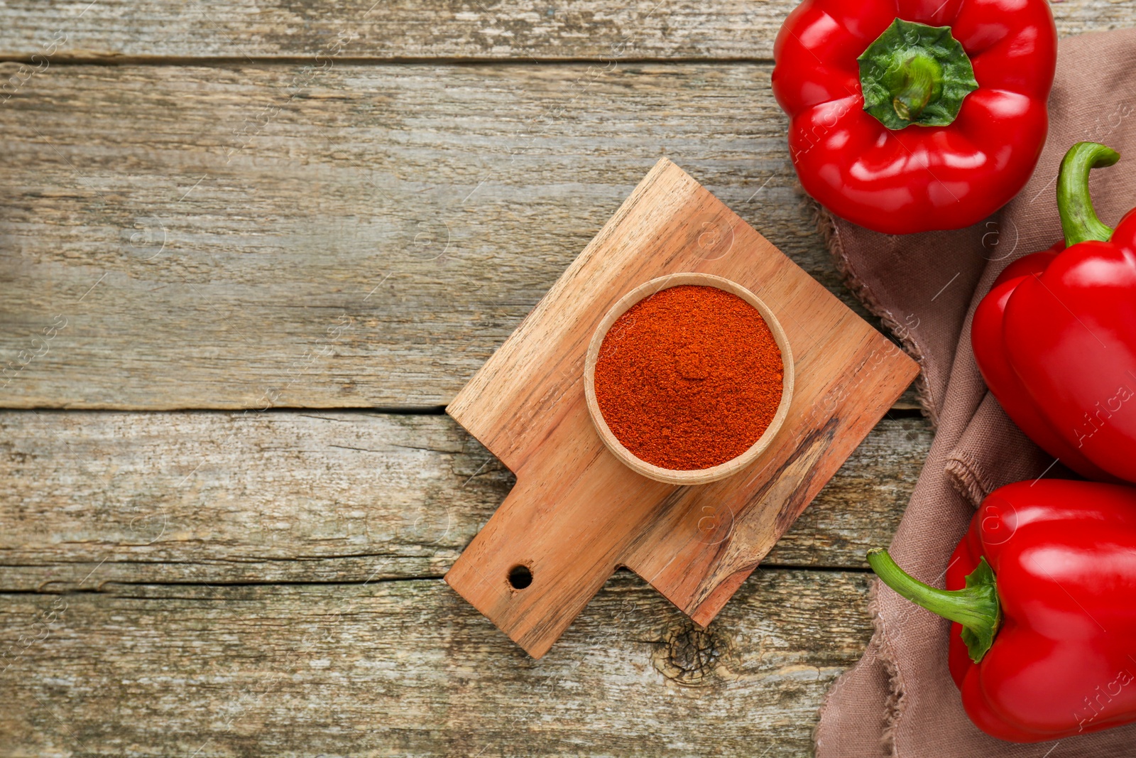 Photo of Bowl with aromatic paprika powder and fresh bell peppers on old wooden table, flat lay. Space for text