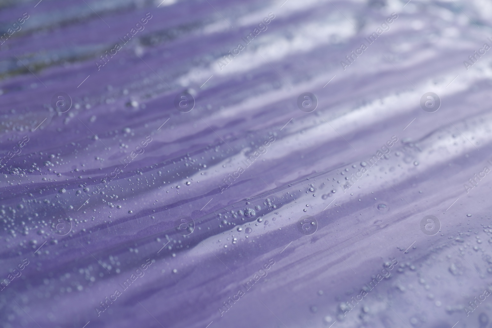 Photo of Texture of transparent shower gel on violet background, closeup