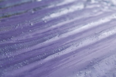 Photo of Texture of transparent shower gel on violet background, closeup