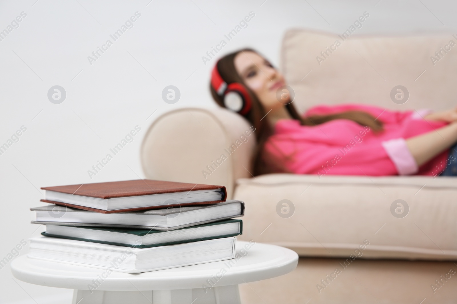 Photo of Stack of books on table at home and woman with headphones on background. Audiobook concept