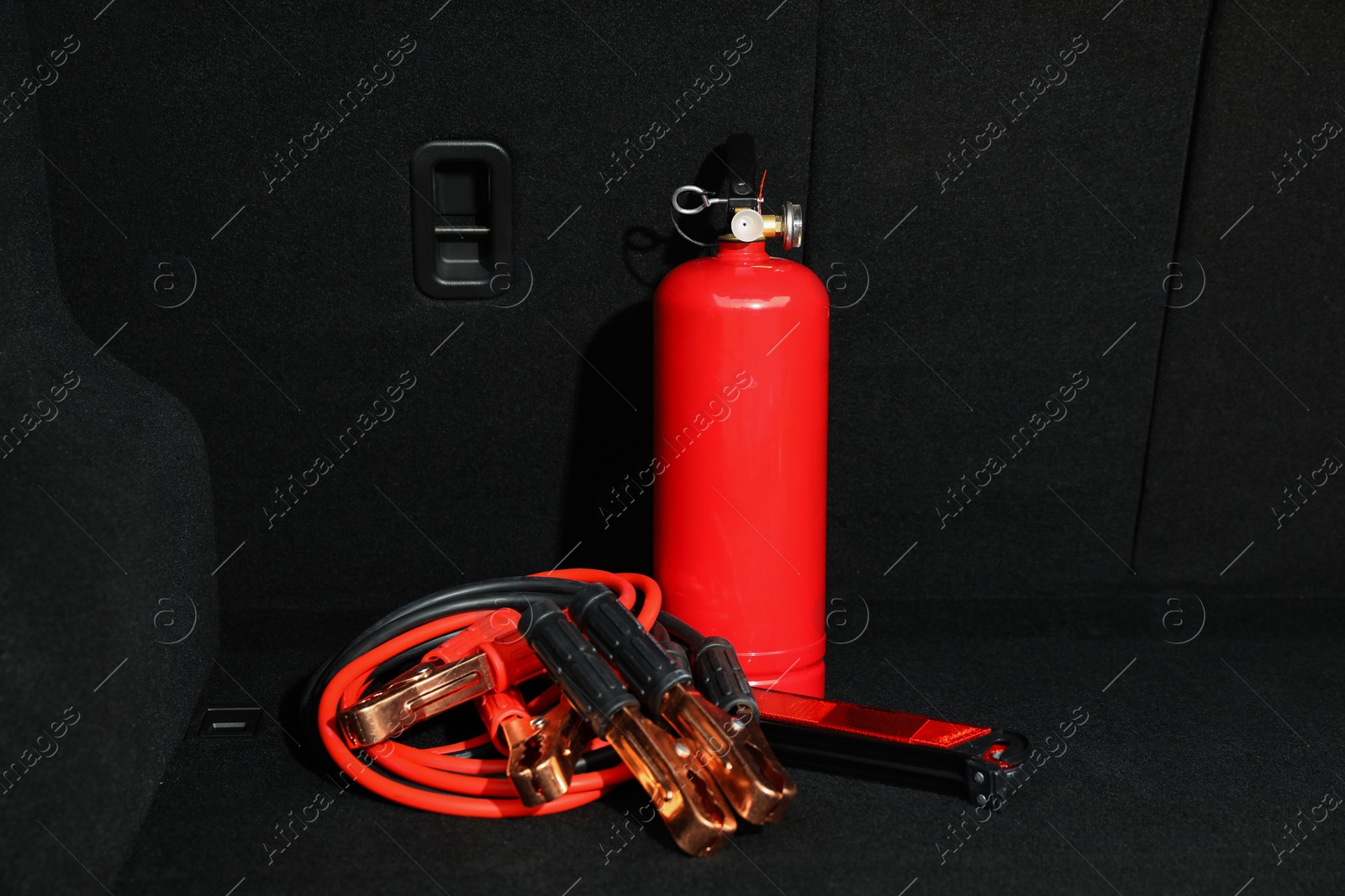 Photo of Red fire extinguisher and battery jumper cables in trunk. Car safety