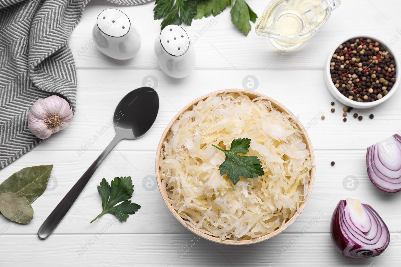 Photo of Bowl of tasty sauerkraut and ingredients on white wooden table, flat lay
