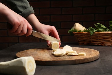 Photo of Woman cutting delicious fresh ripe parsnip at black table, closeup