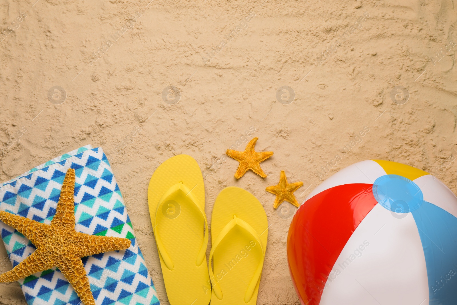 Photo of Colorful beach ball, blanket, flip flops and starfishes on sand, flat lay. Space for text