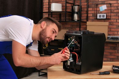 Repairman with screwdriver fixing coffee machine at table indoors