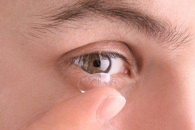 Young man putting contact lens in his eye, closeup