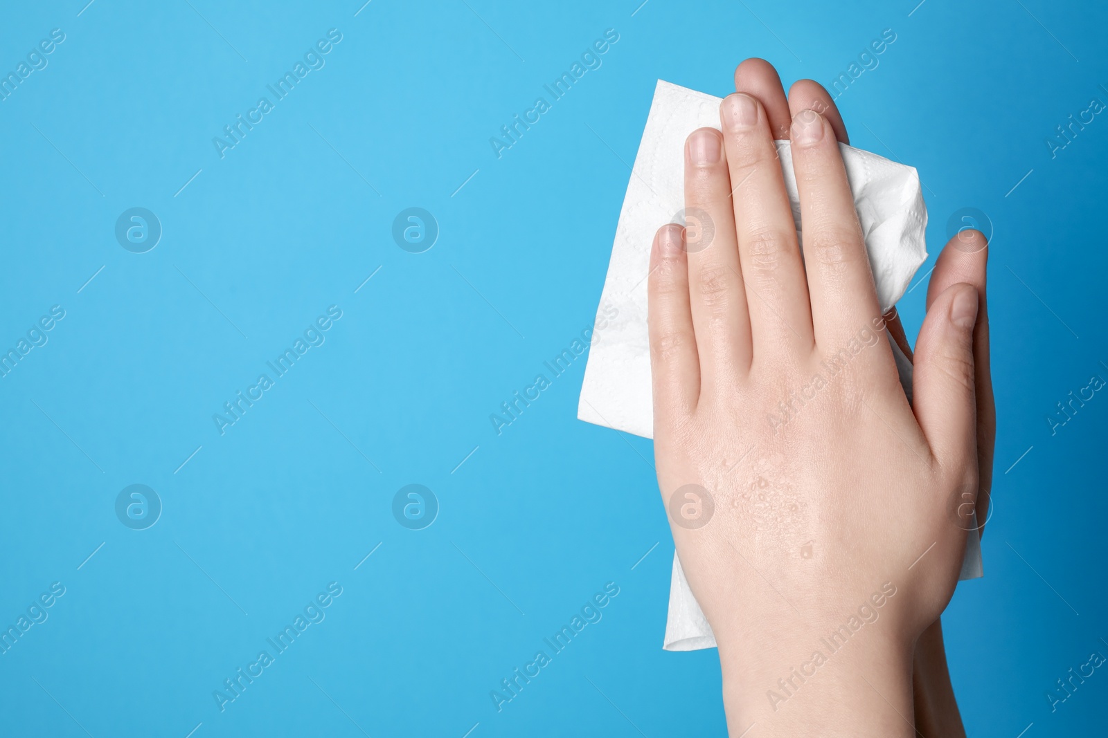 Photo of Woman wiping hands with paper towel on light blue background, closeup. Space for text