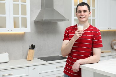 Photo of Happy man with milk mustache holding glass of tasty dairy drink in kitchen