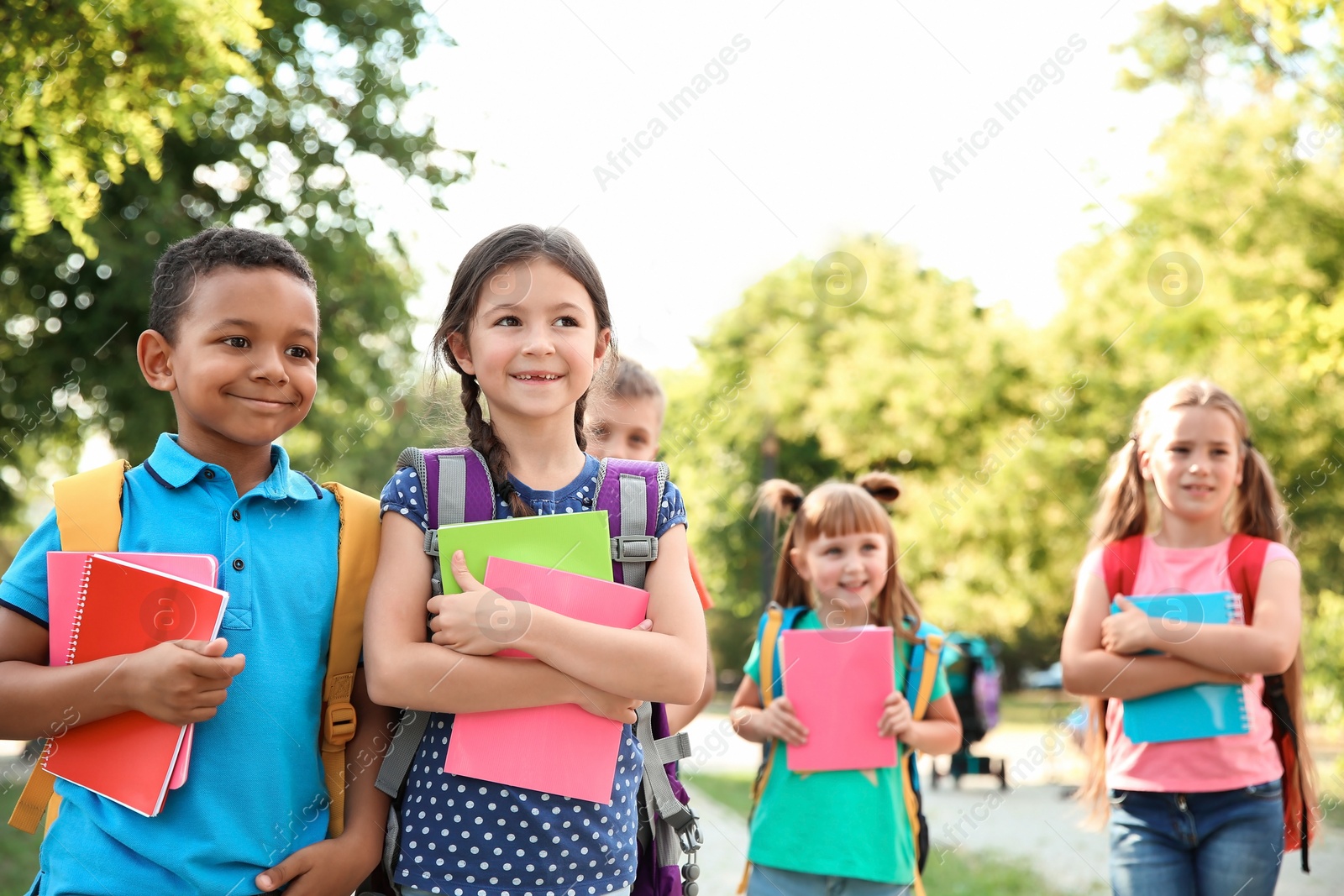 Photo of Cute little children with backpacks and notebooks outdoors. Elementary school