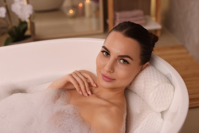 Photo of Young woman using pillow while enjoying bubble bath indoors