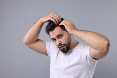 Man examining his head on light grey background. Dandruff problem