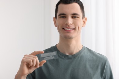 Young man with whitening strips on light background. Space for text