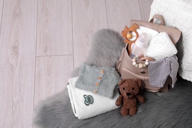 Photo of Mother's bag with baby's stuff on floor indoors. Space for text